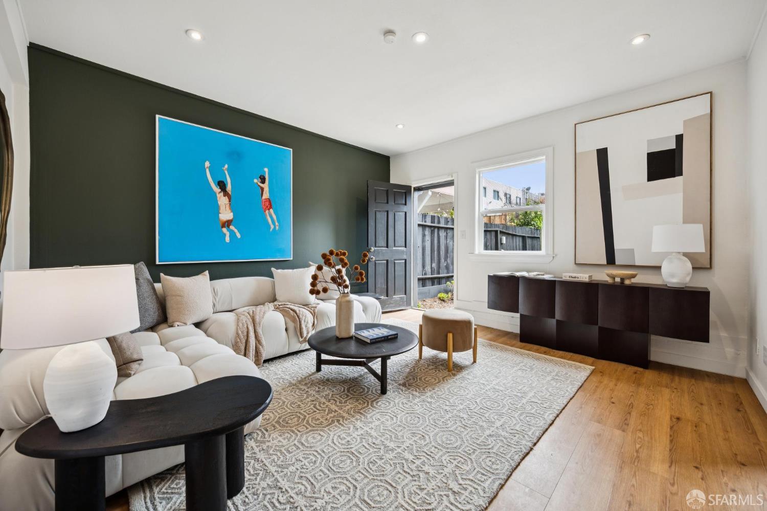 Staged living room with a white sectional, dark green accent wall, and door opening to a fenced yard.
