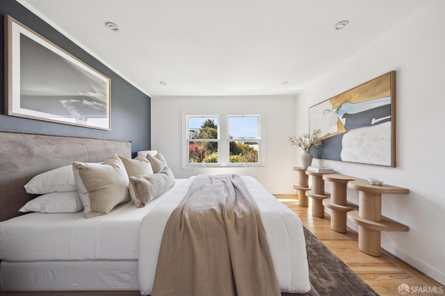 Staged bedroom with a large white bed, dark accent wall, abstract art, and hardwood floors.