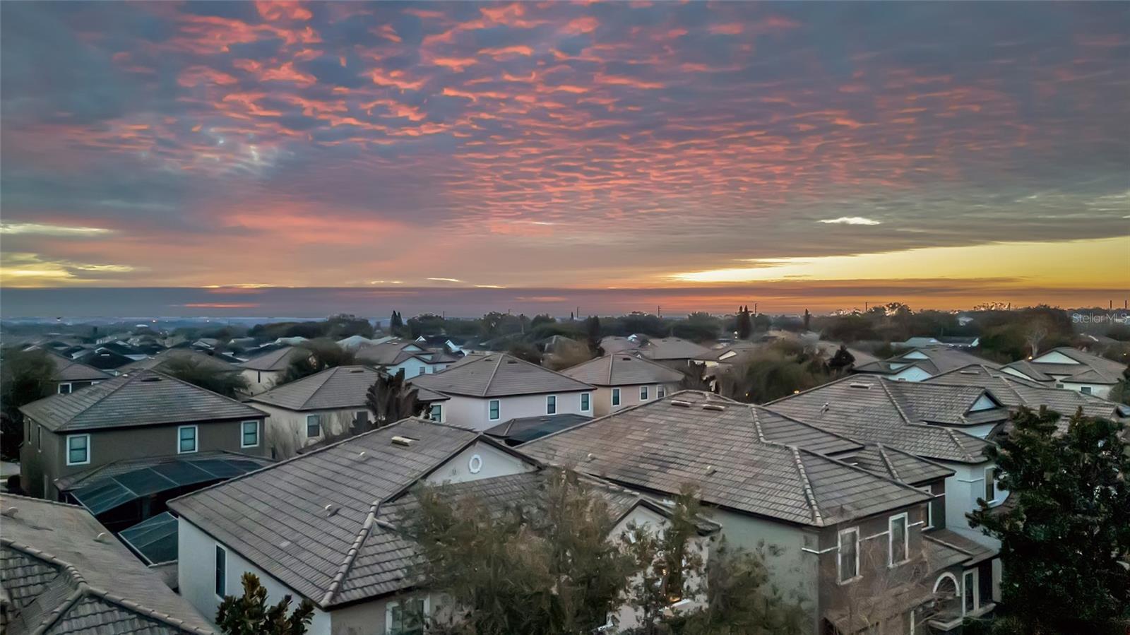 Aerial view of a residential neighborhood beneath a vivid pink and orange sunset.