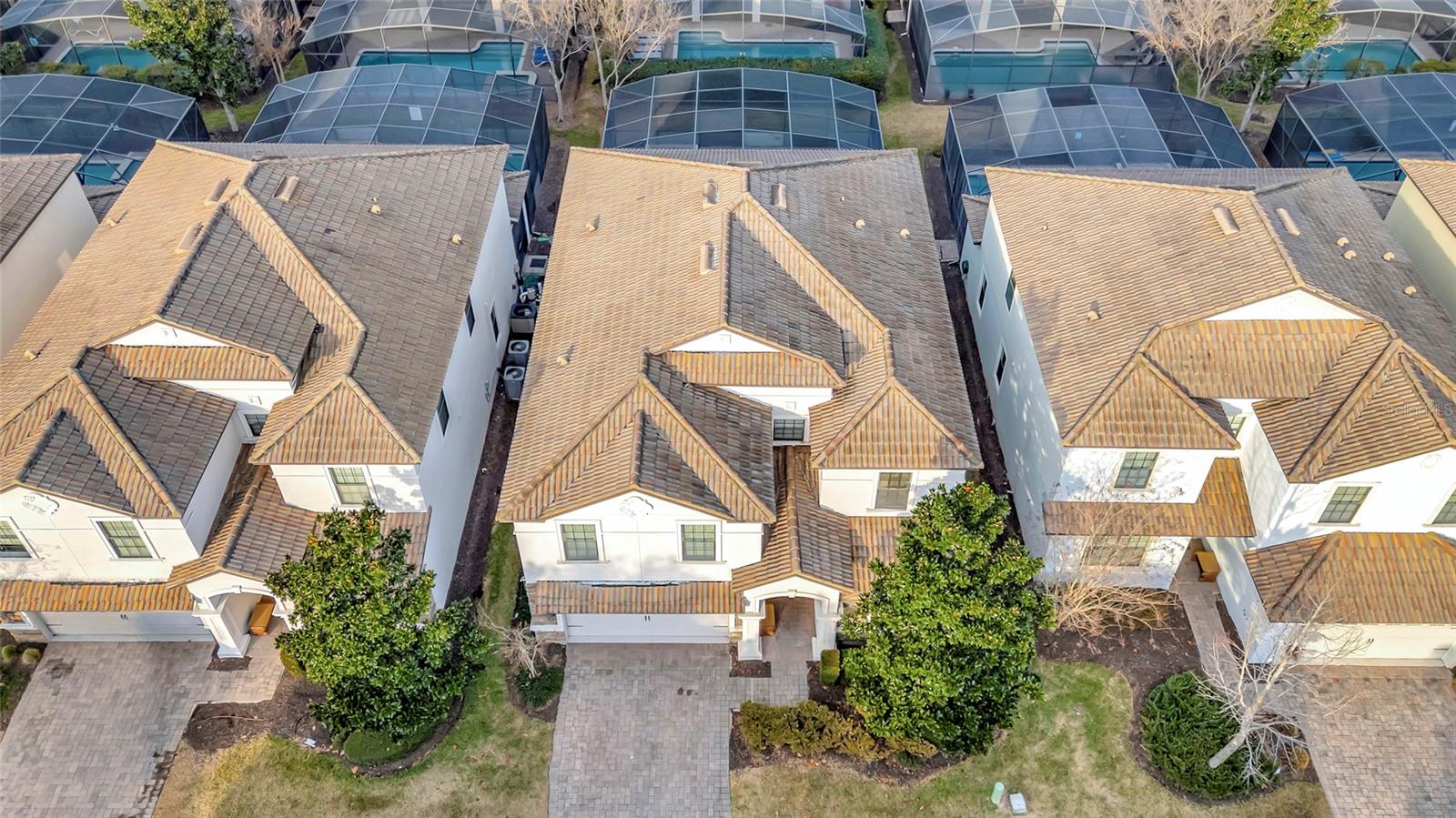 Aerial view of neighboring homes with tile roofs, screened pool enclosures, and front driveways.