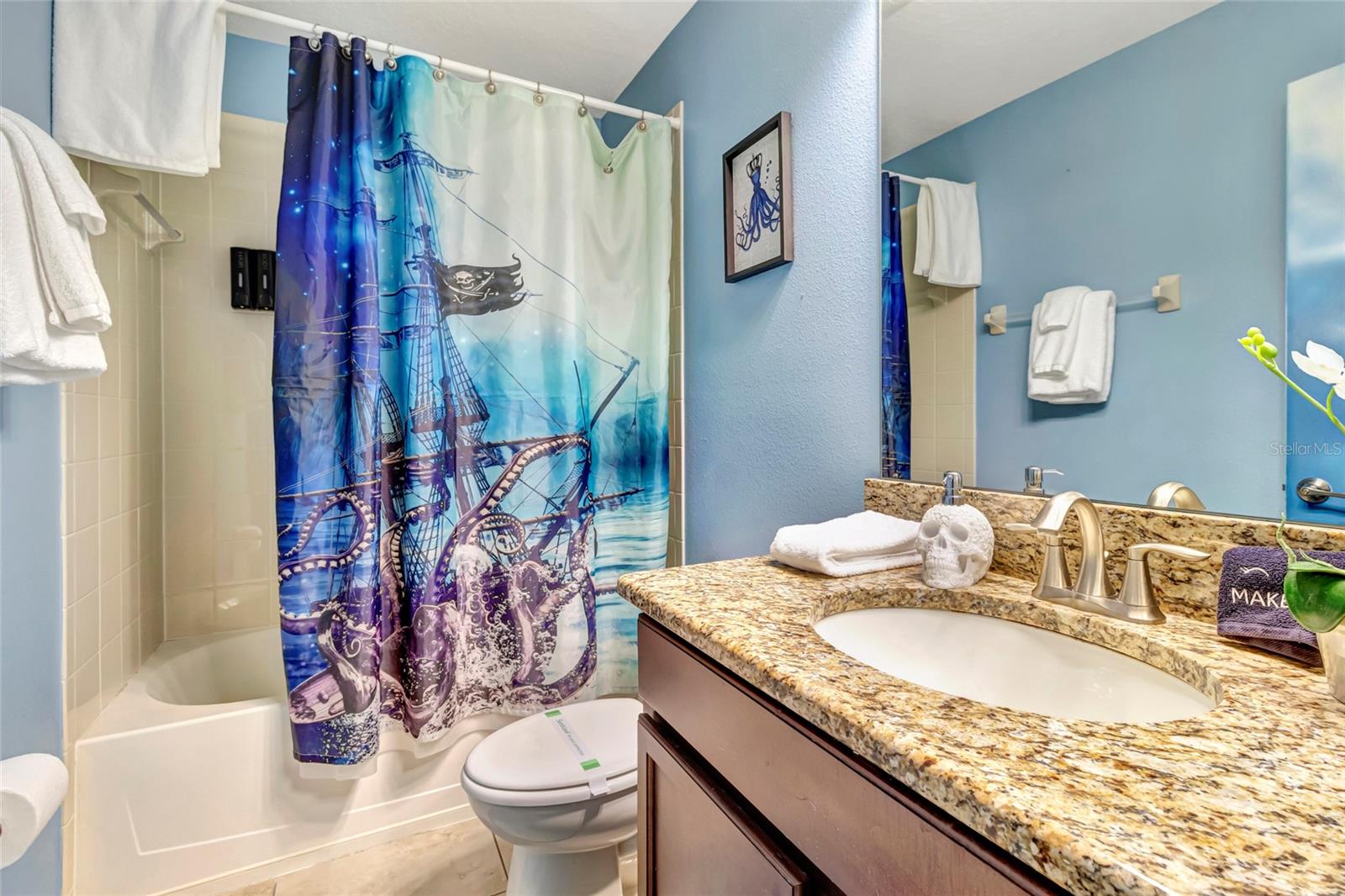 Bathroom with a blue pirate ship shower curtain and granite vanity.
