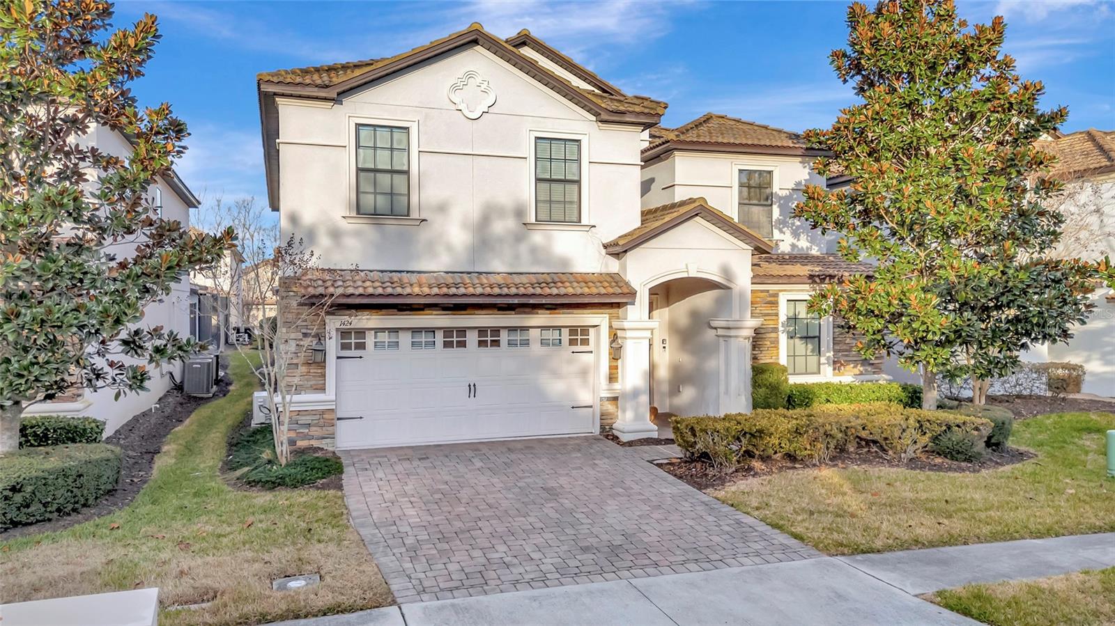 Two-story stucco home with a tiled roof, arched entry, stone accents, and a paver driveway.