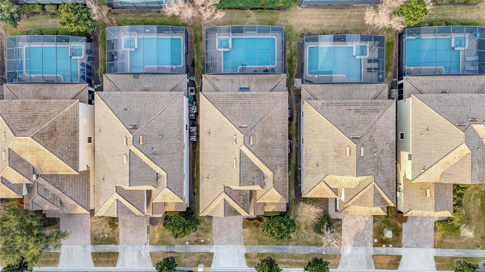 Aerial view of neighboring homes with screened backyard pools and tiled roofs.