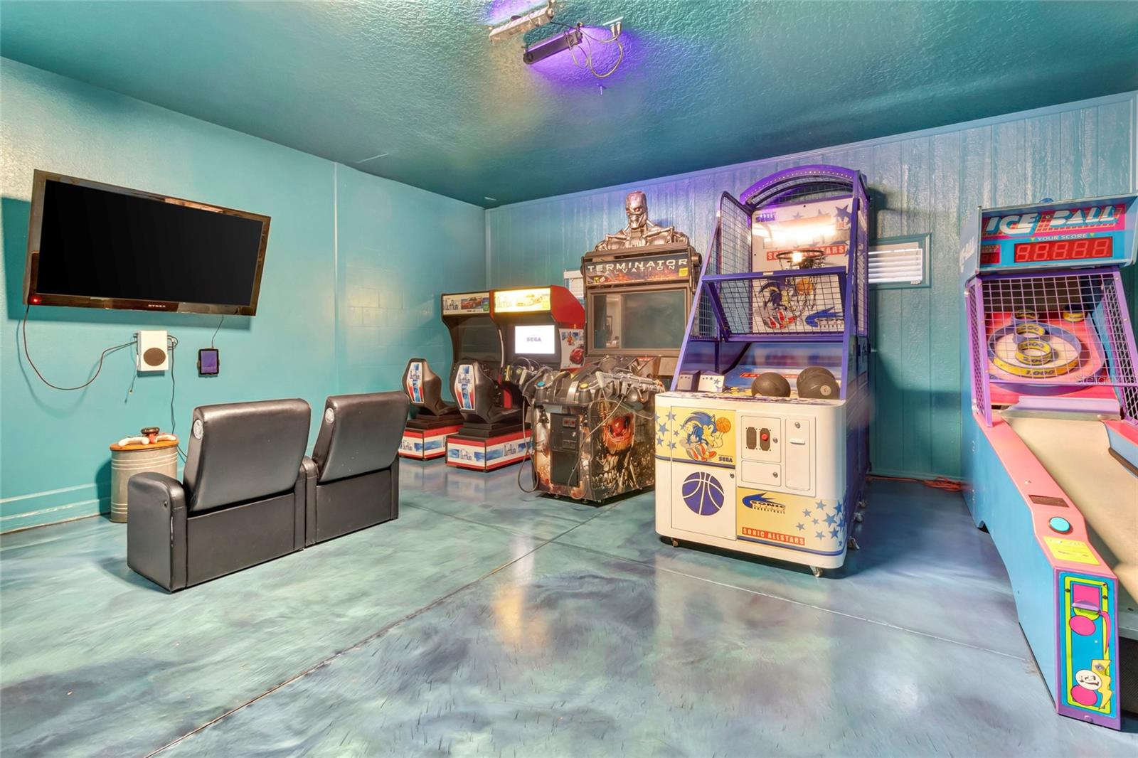 Arcade game room with basketball machines, an air hockey table, and rows of arcade cabinets.
