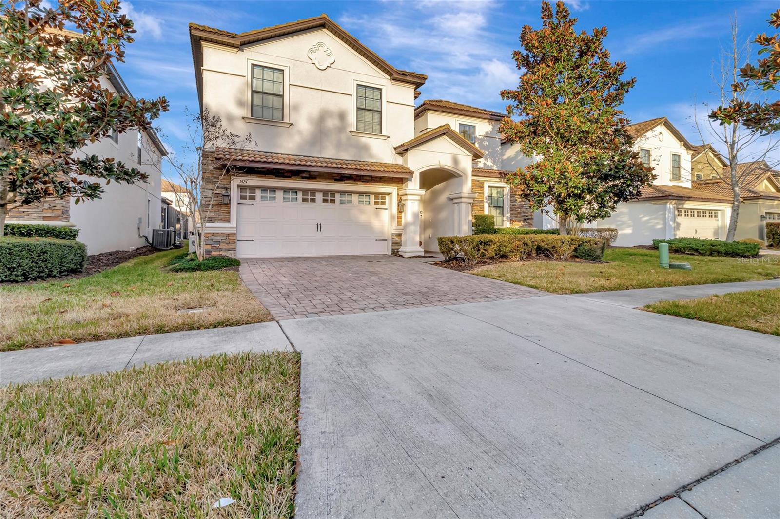 Two-story cream stucco home with stone accents, an arched entry, and a double garage.