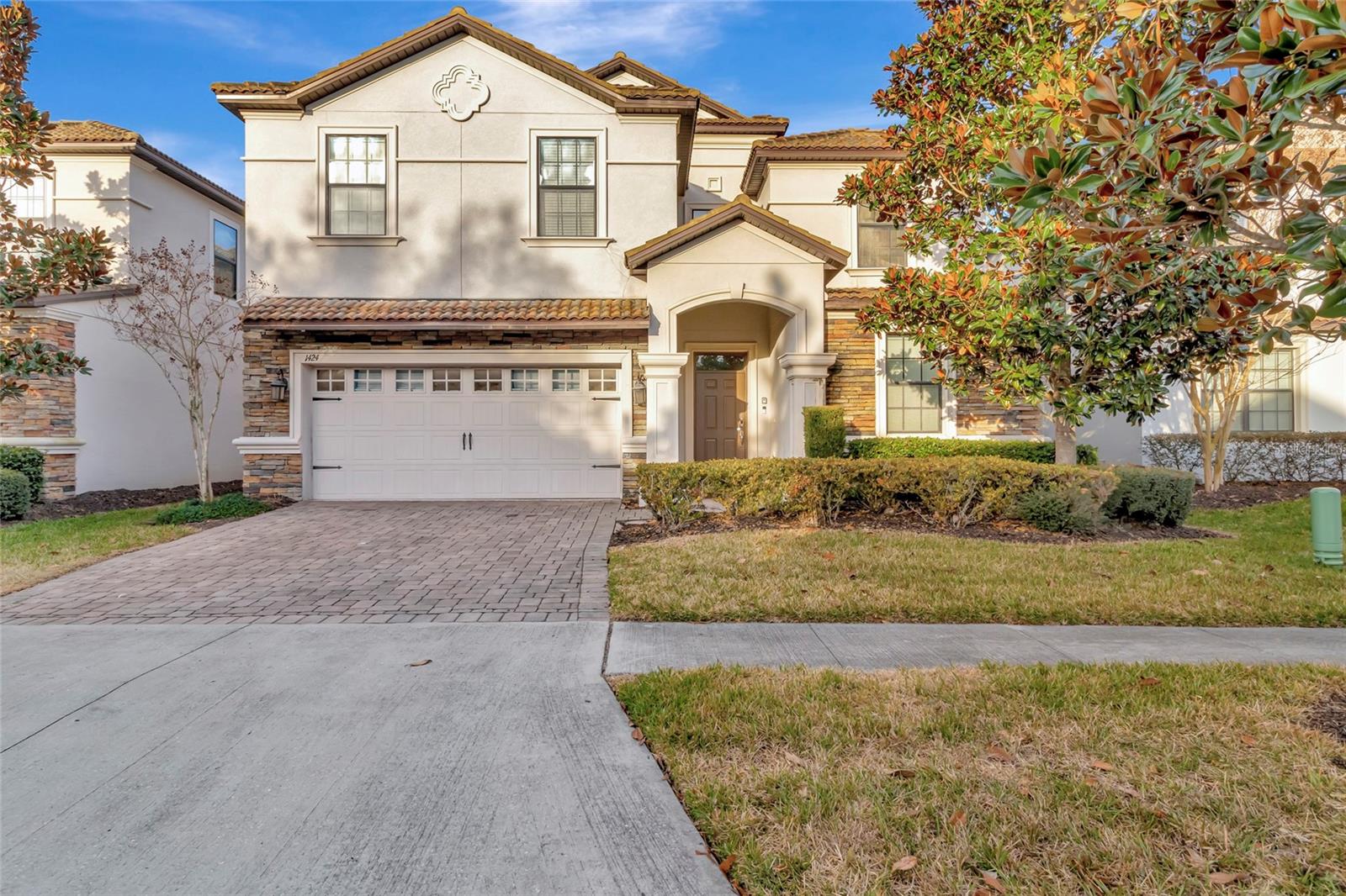 Two-story stucco house with stone accents, a tile roof, and a two-car garage.