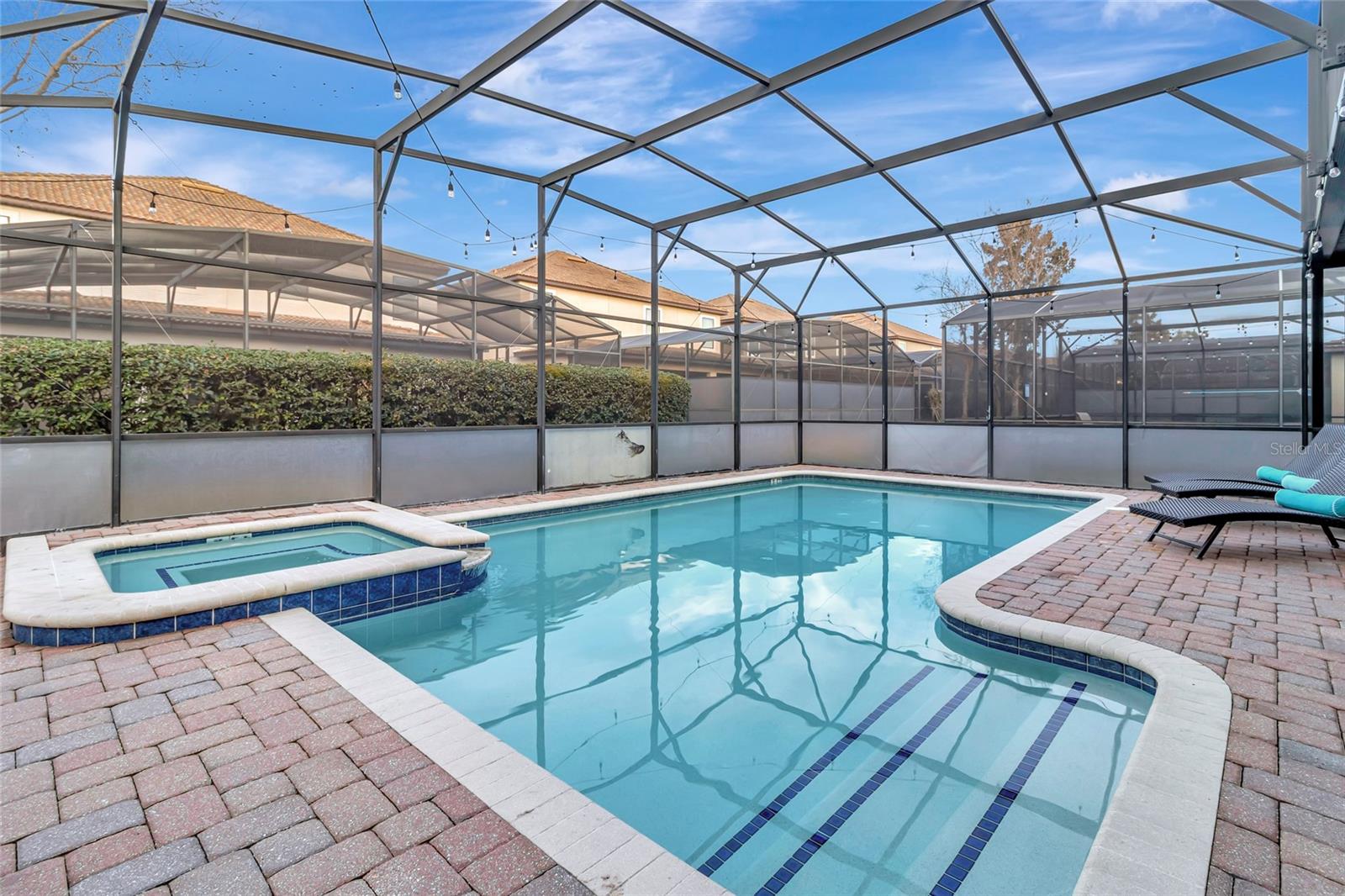 Screened backyard pool with an attached spa, paver deck, and lounge chairs.
