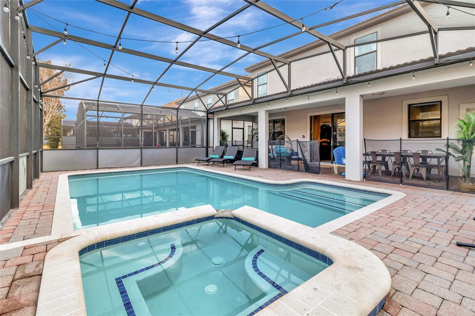 Backyard pool and spa under a screened enclosure, with paver decking and patio seating.