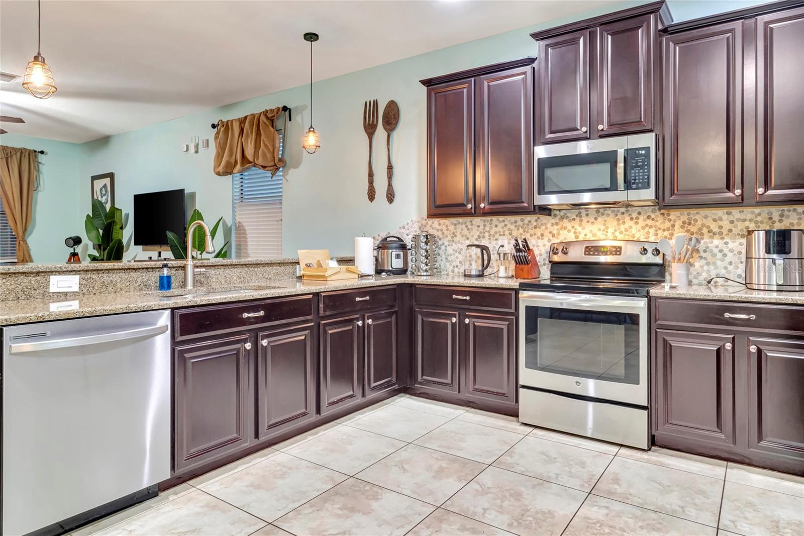 Kitchen with dark wood cabinets, granite counters, mosaic backsplash, and stainless steel appliances.