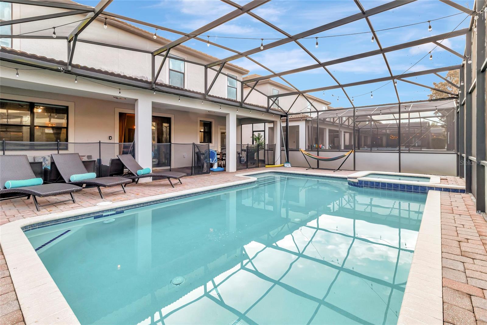 Screened swimming pool and raised spa beside a two-story home, with lounge chairs and a hammock.