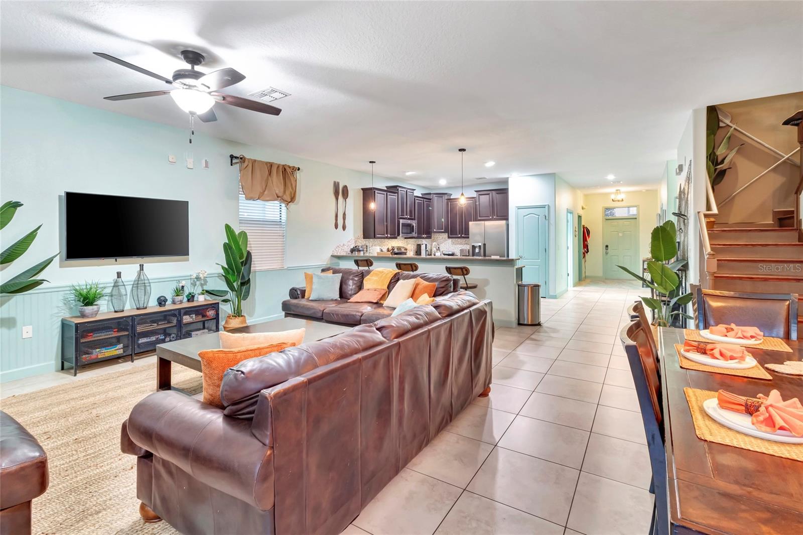 Open-plan living room and kitchen with brown leather sofas, a kitchen island, and adjoining dining area.