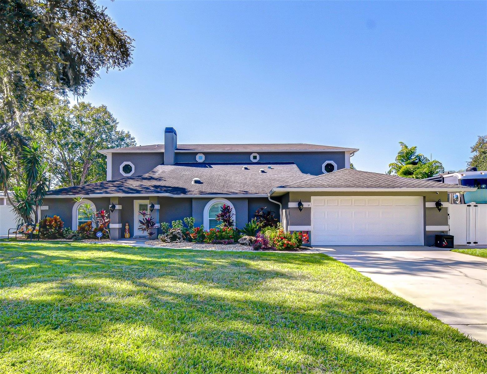 Dark gray home with round windows, a white garage door, and colorful landscaping.