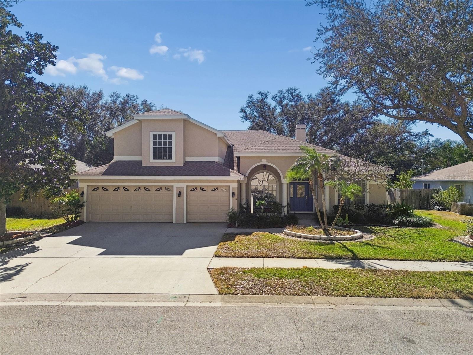 Two-story beige home with a three-car garage, arched entry, and landscaped front yard.