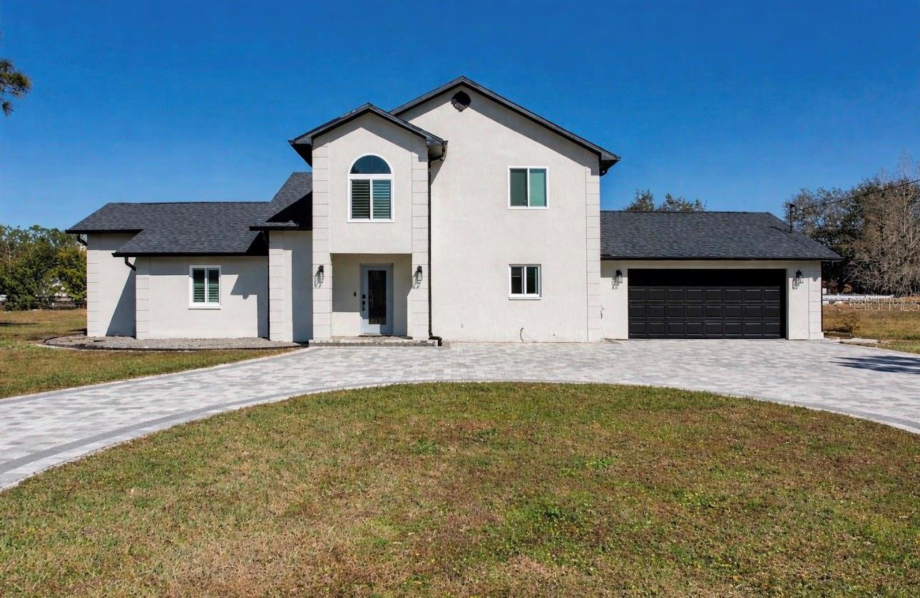 Two-story white stucco home with an arched window and broad paved driveway.