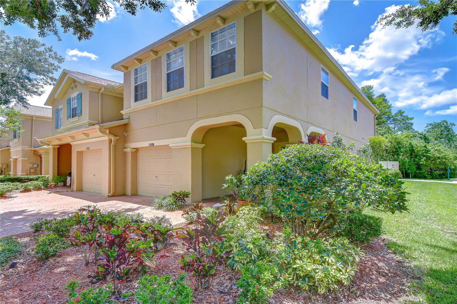Tan two-story townhouse with an arched entry, attached garage, and landscaped front garden.