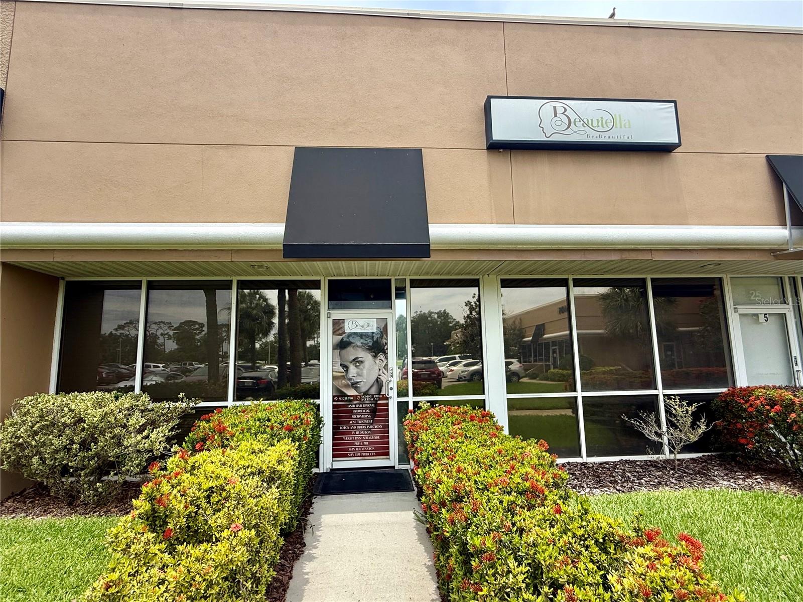 Commercial storefront with a Beautella sign, glass windows, and landscaped entrance.