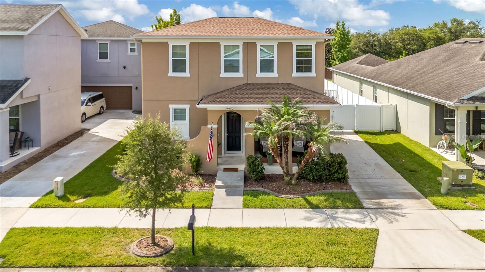 Tan two-story house with a covered porch, palm trees, and neighboring homes