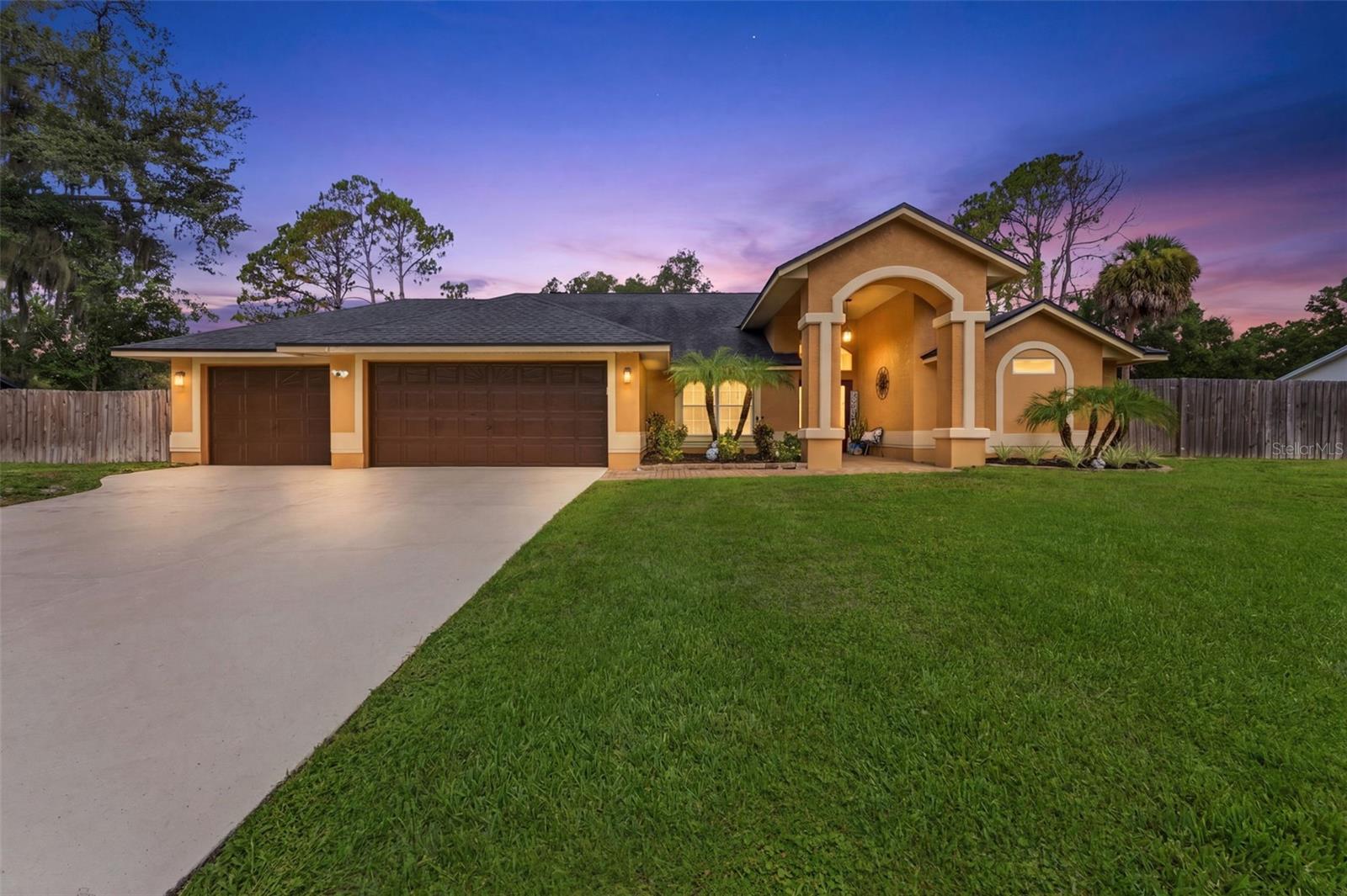 Tan stucco home with an arched entry and two-car garage at dusk.