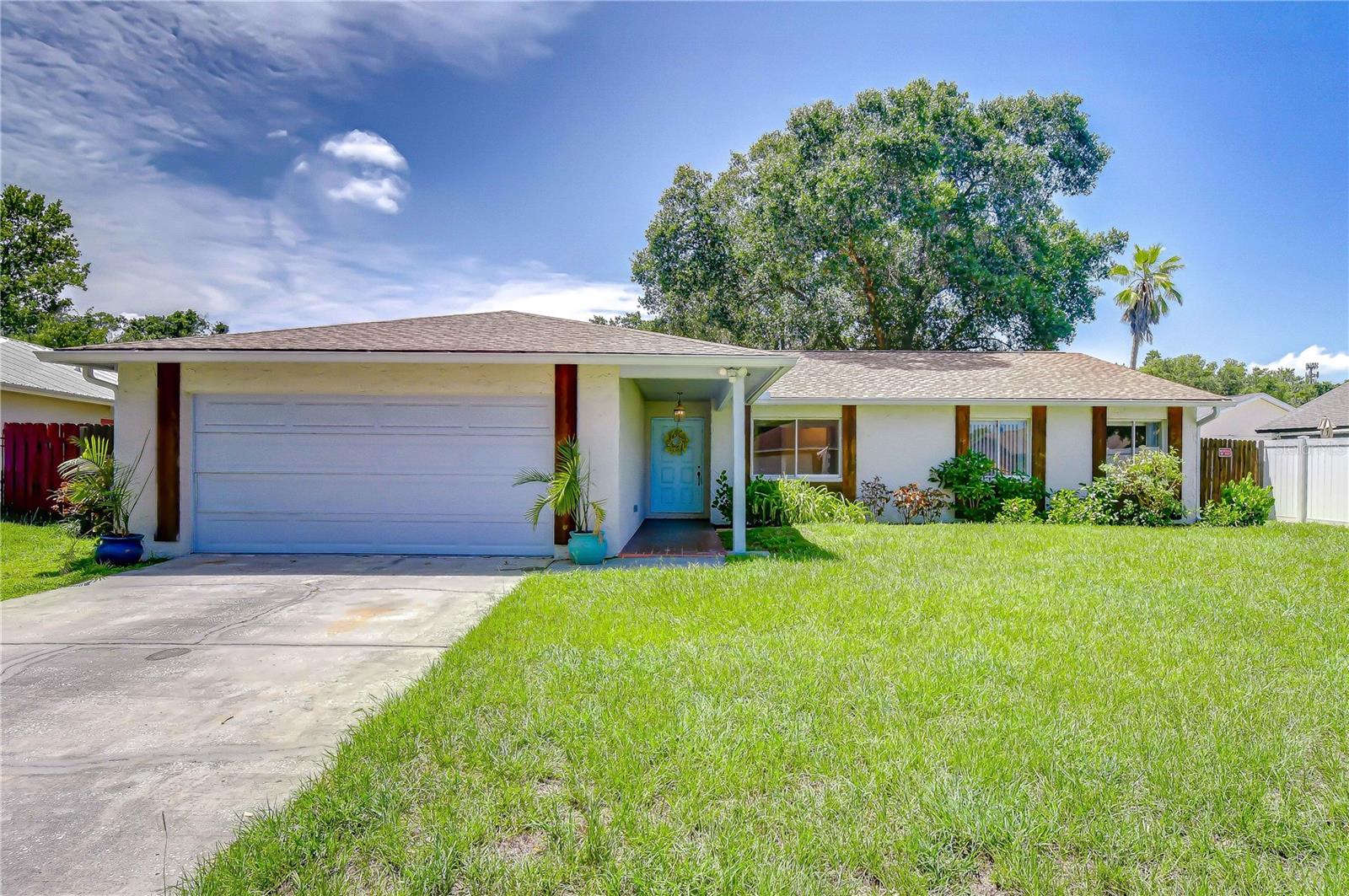 Single-story home with a two-car garage, turquoise front door, and broad green lawn.