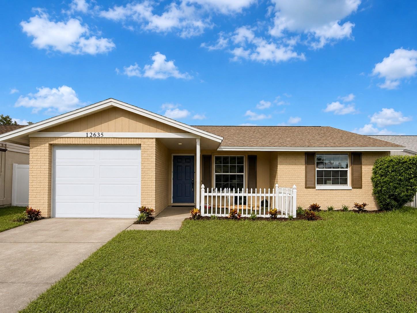 Single-story beige brick ranch house with a white garage door and small white picket fence.