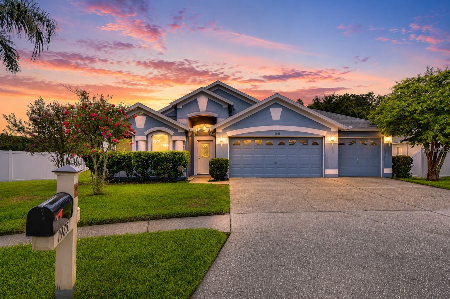 Blue-gray single-story home with a three-car garage and landscaped lawn at dusk.
