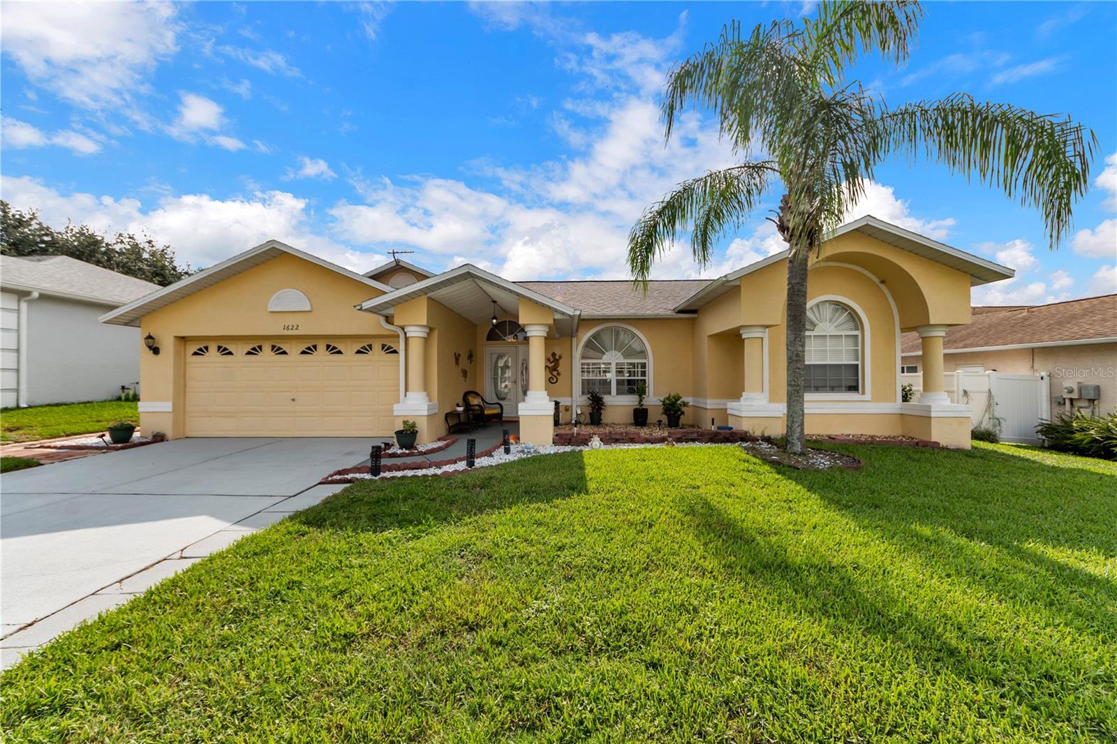 Yellow single-story home with a two-car garage, arched windows, and a palm tree in the front lawn.