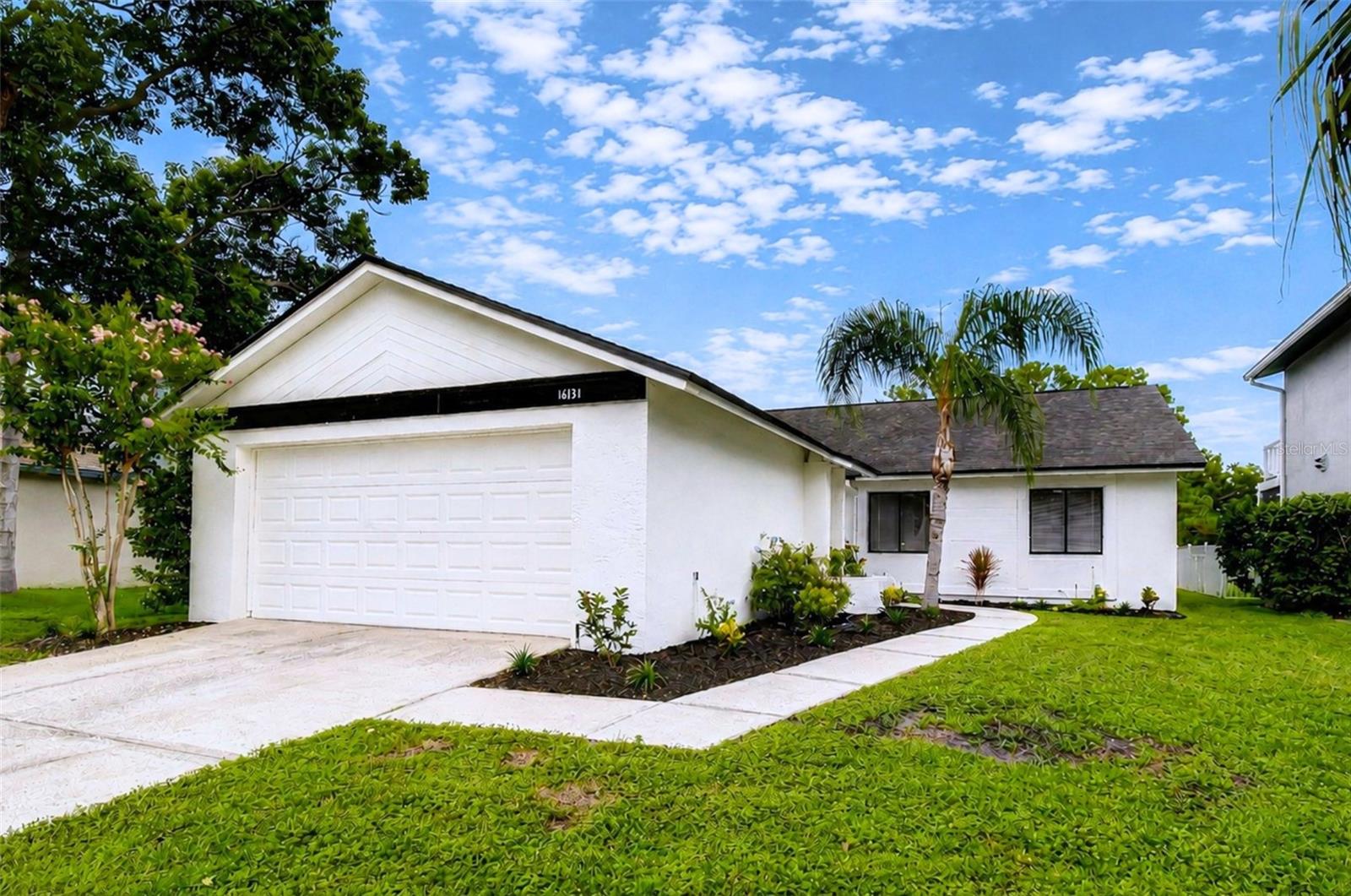 White single-story house with a two-car garage, palm trees, and a curved front walkway.
