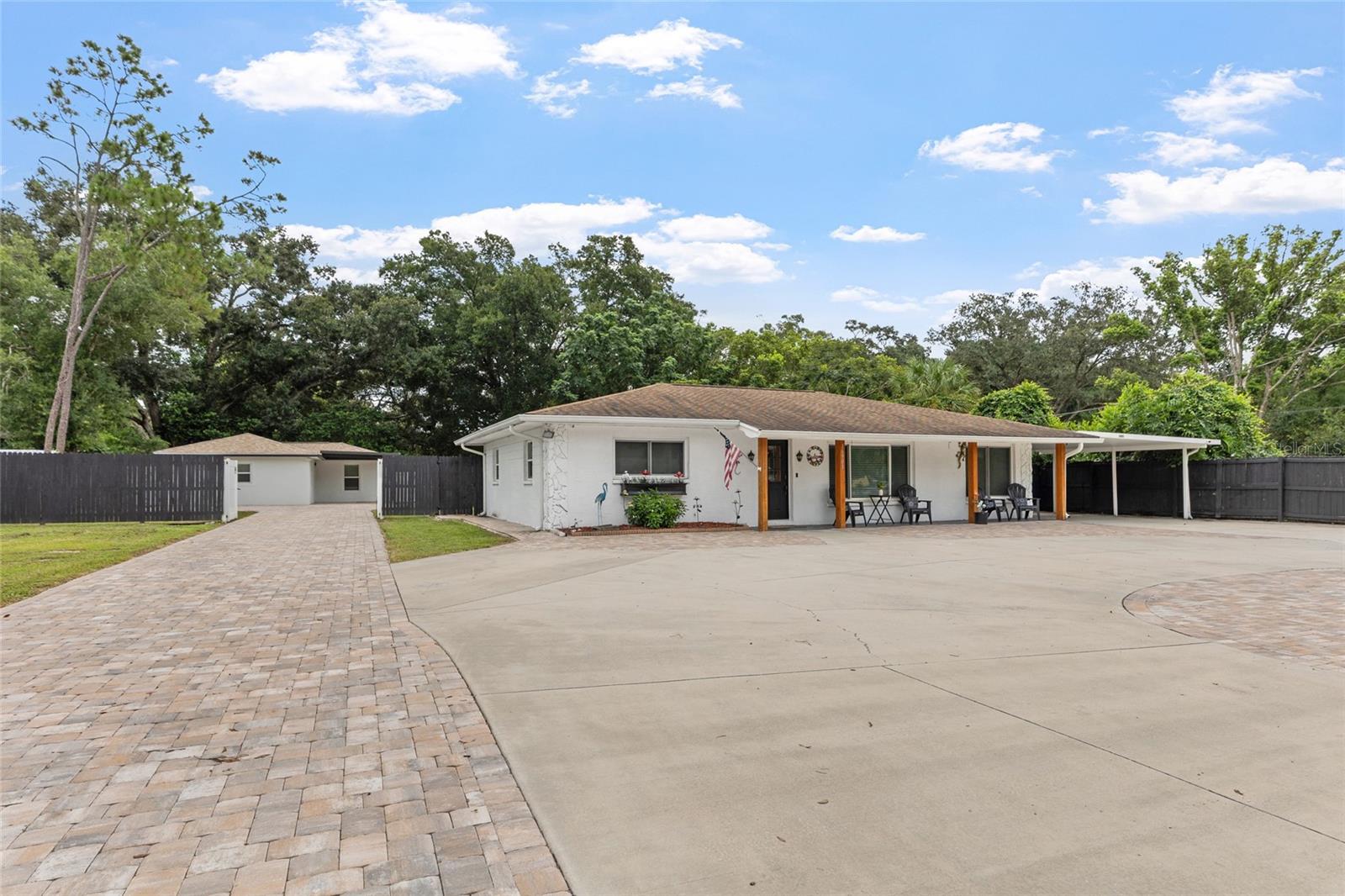 Single-story white home with a broad driveway, paver walkway, detached garage, and covered carport.