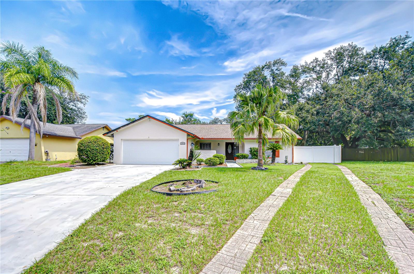 Single-story home with a double garage, palm trees, broad driveway, and paved walkway.