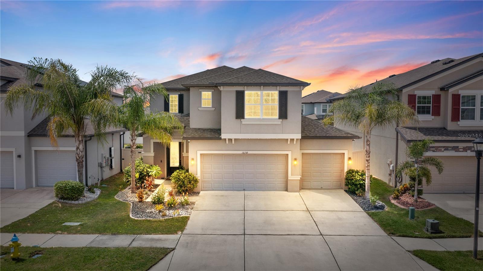 Two-story stucco home with a three-car garage and palm-lined landscaping at sunset.