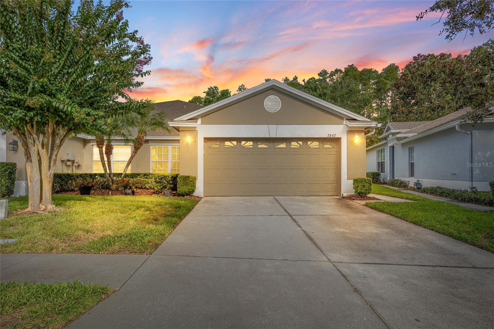 Single-story beige house with a double garage and landscaped lawn beneath a colorful dusk sky.