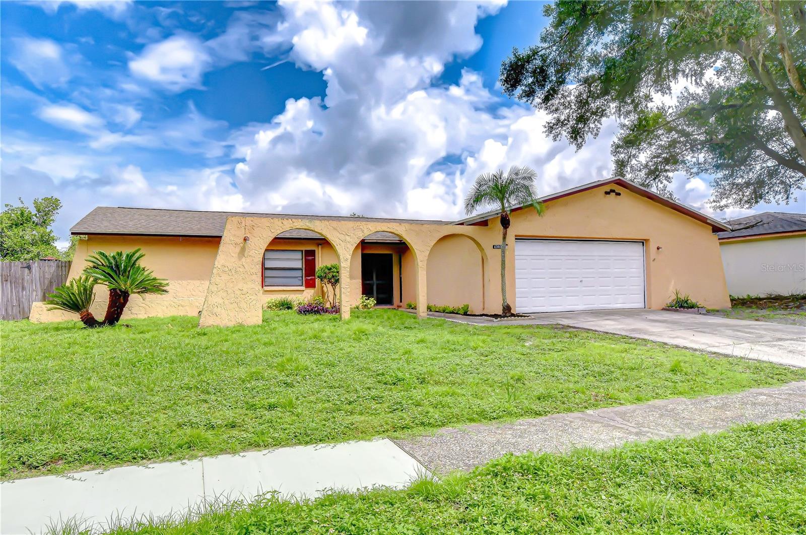 Single-story peach stucco home with arched entryways, a white double garage door, and a front lawn.