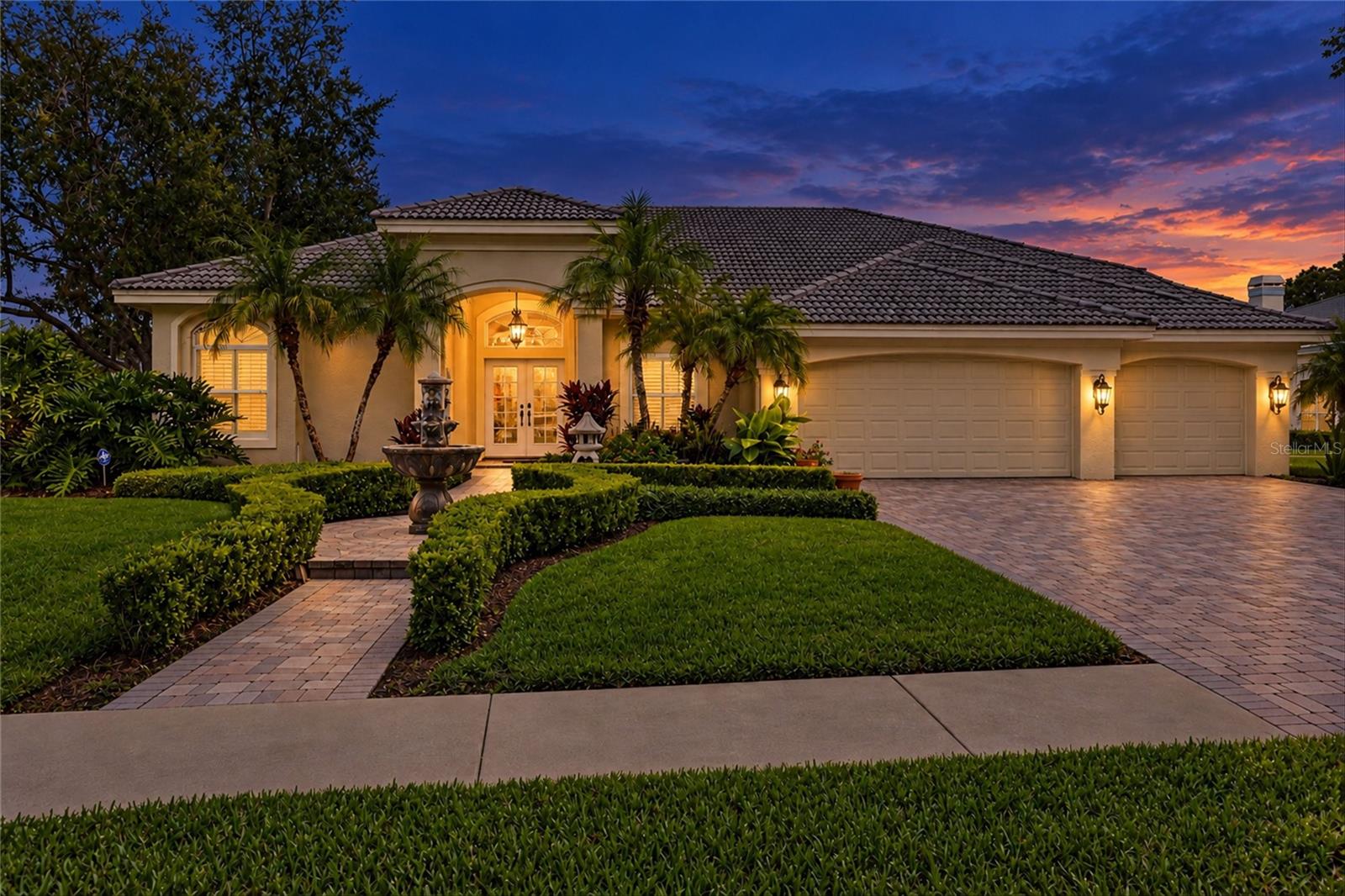 Stucco home with a tile roof, landscaped grounds, and illuminated entry at dusk.