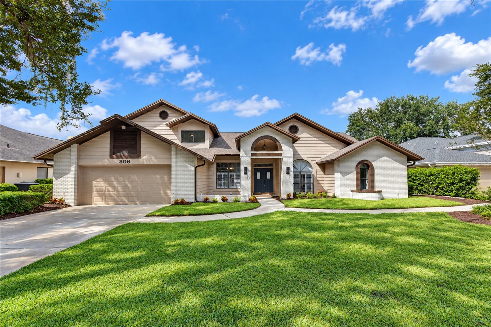 Home exterior with white brick accents, an arched entryway, two-car garage, and green lawn.