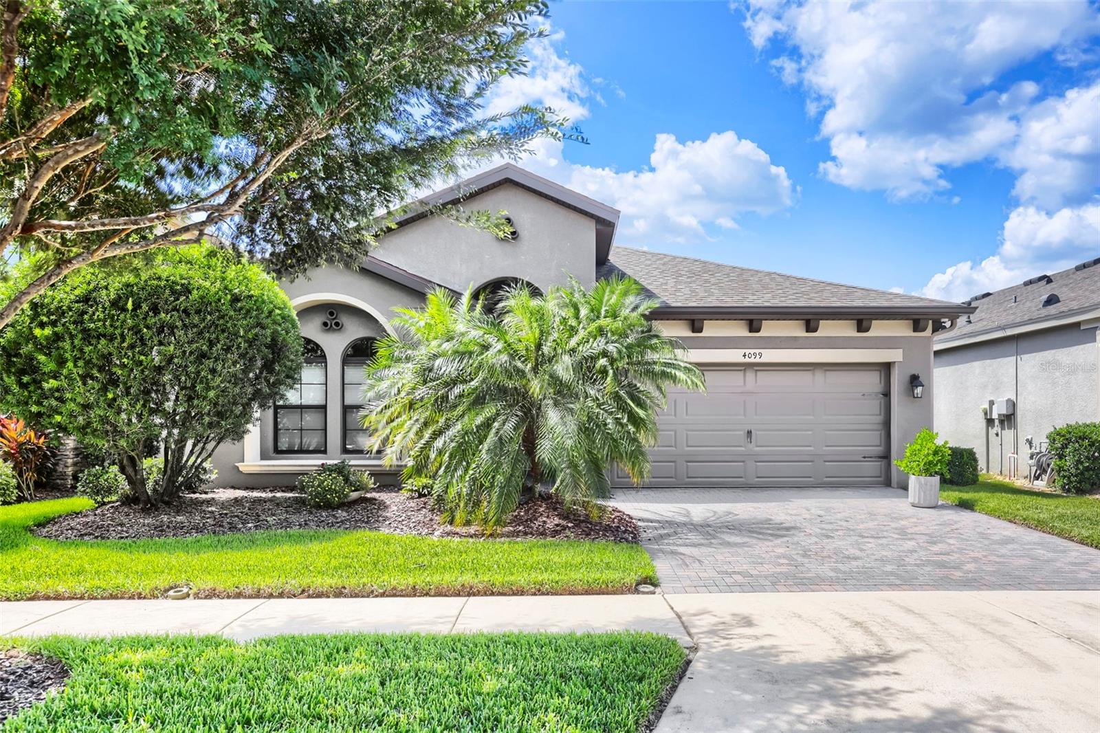 Gray stucco home with arched windows, a two-car garage, and palm trees in the front yard.