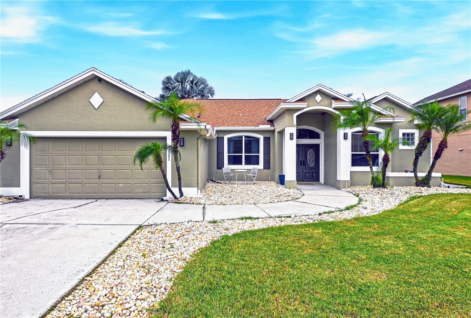 Single-story Florida home with an arched entry, two-car garage, palm trees, and stone landscaping.