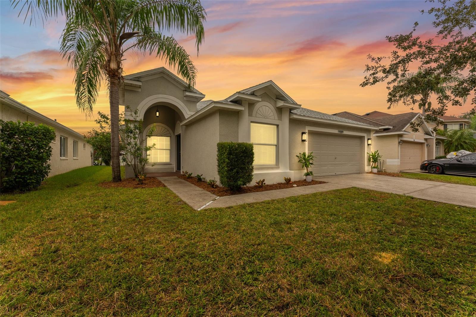 Stucco home with arched entry and two-car garage beneath a colorful sunset.