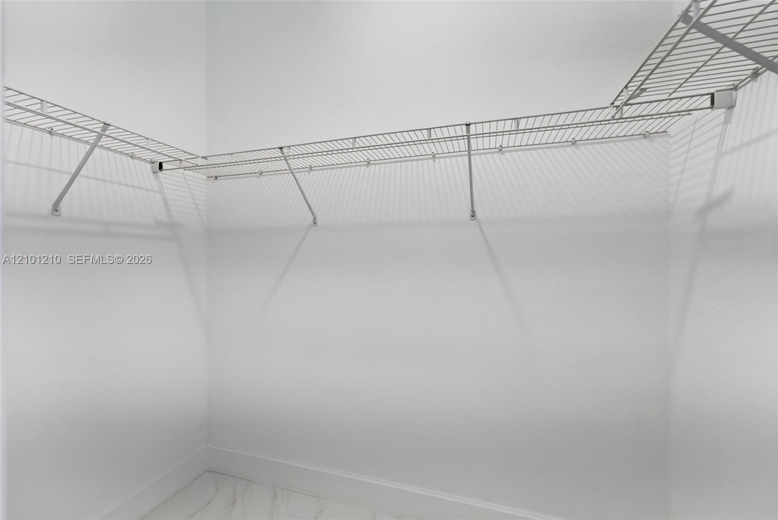 Empty walk-in closet with wraparound wire shelving and hanging rods.