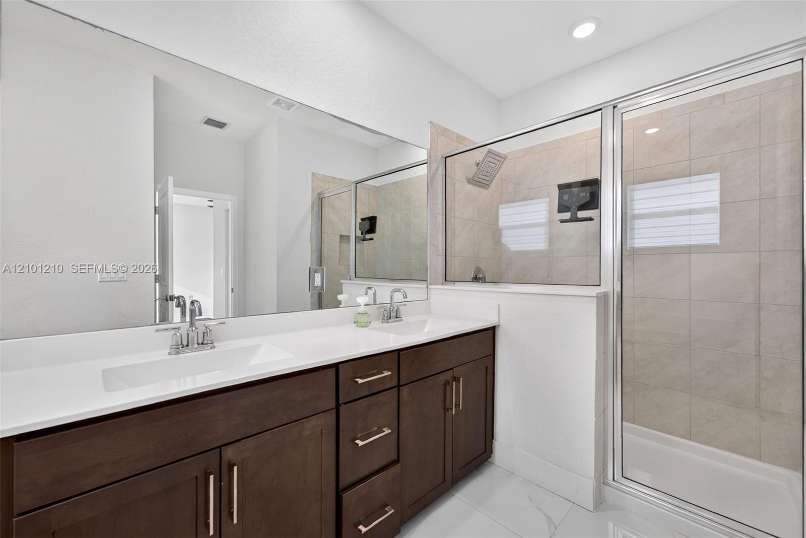 Bathroom with a dark double vanity, large mirror, and glass-enclosed tiled shower.