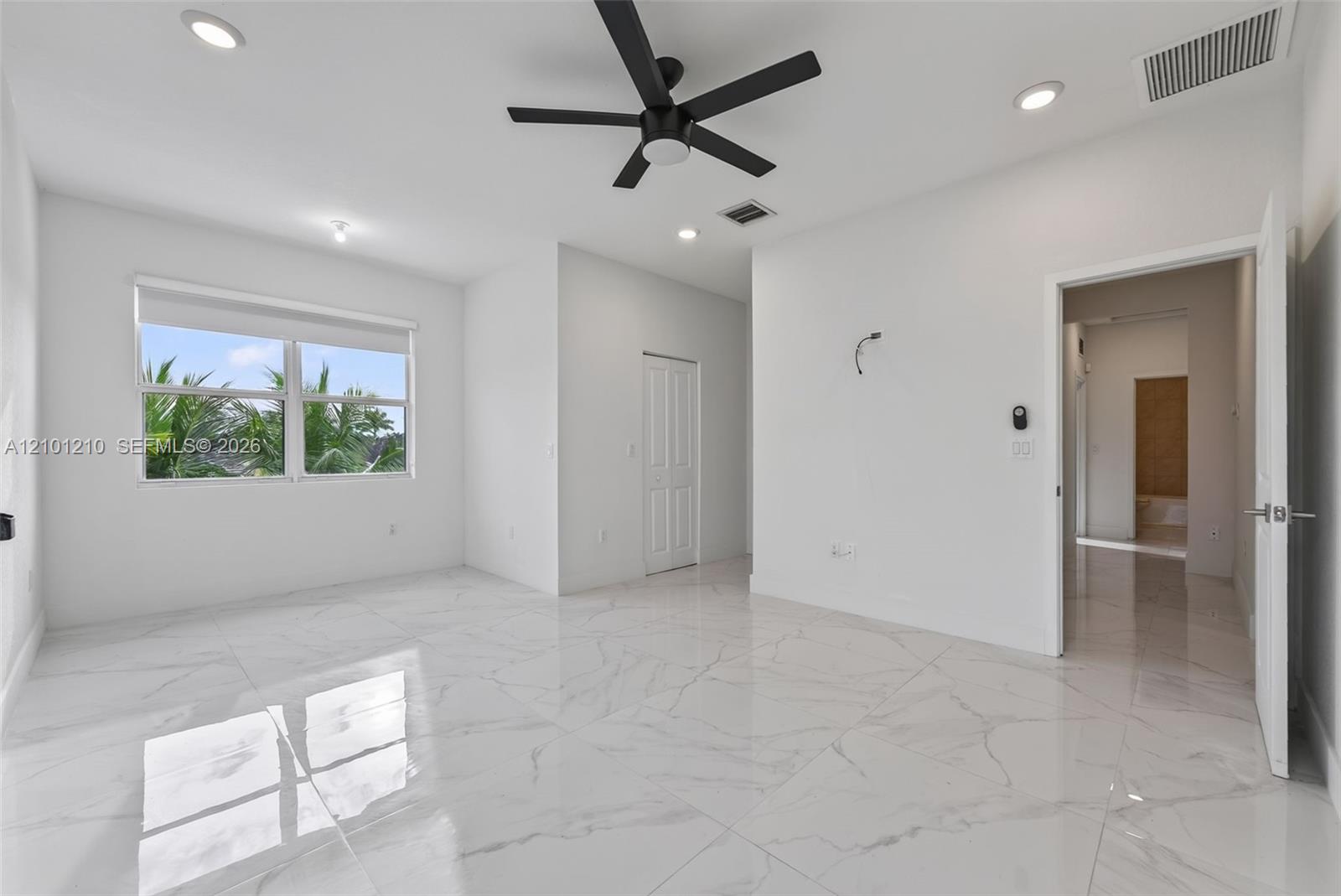 Vacant bedroom with glossy marble-look tile floors, a black ceiling fan, and a window overlooking palm trees.