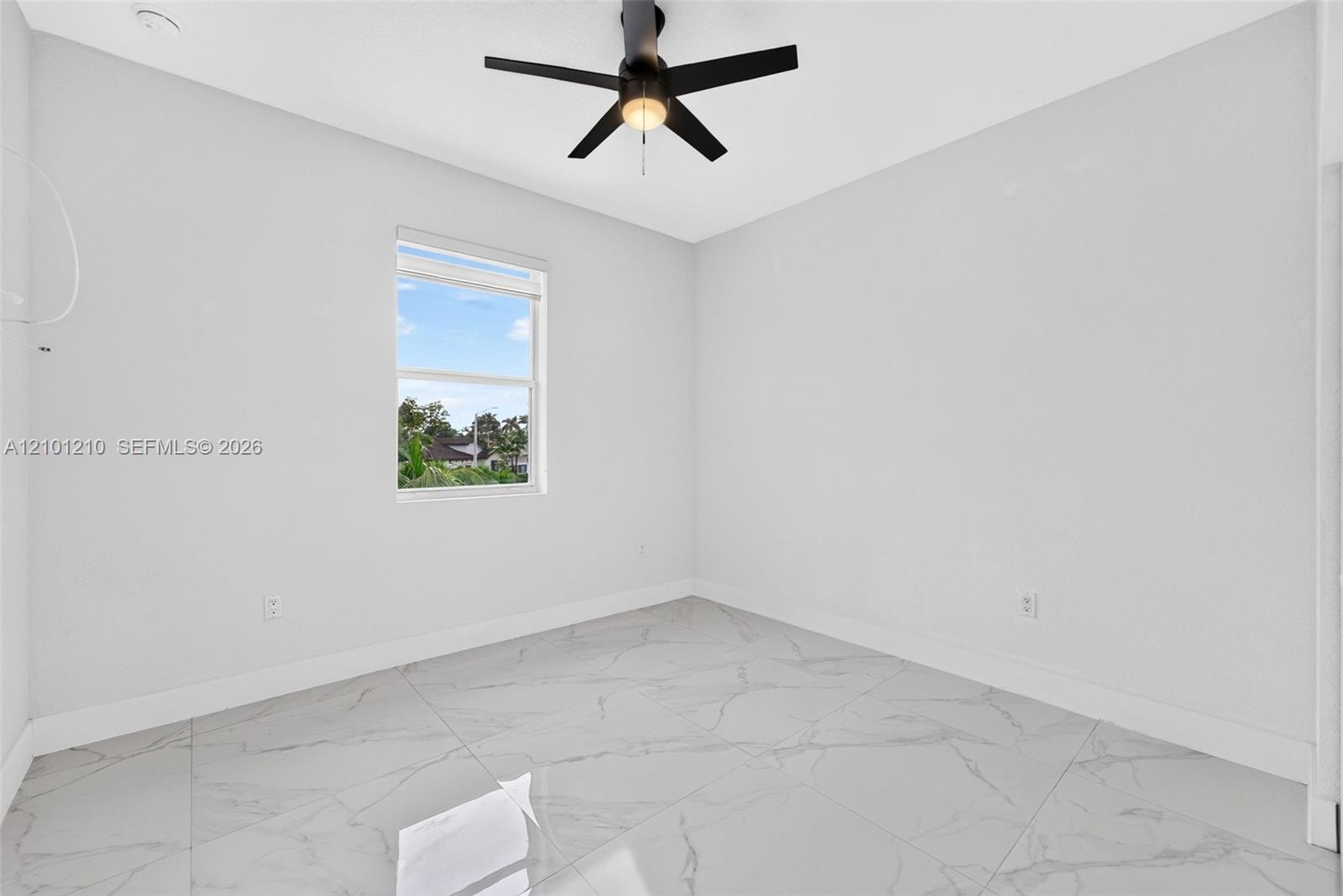 Empty room with marble-look tile floors, a black ceiling fan, and a window overlooking greenery.