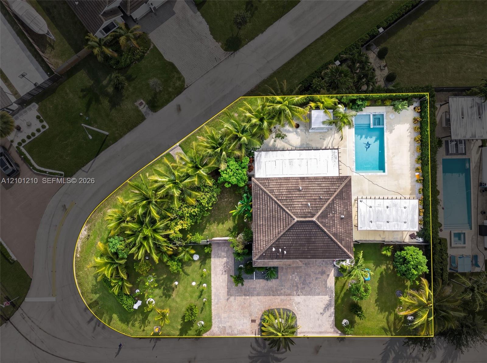 Aerial view of a home with a backyard pool, tropical landscaping, and a yellow-outlined lot.