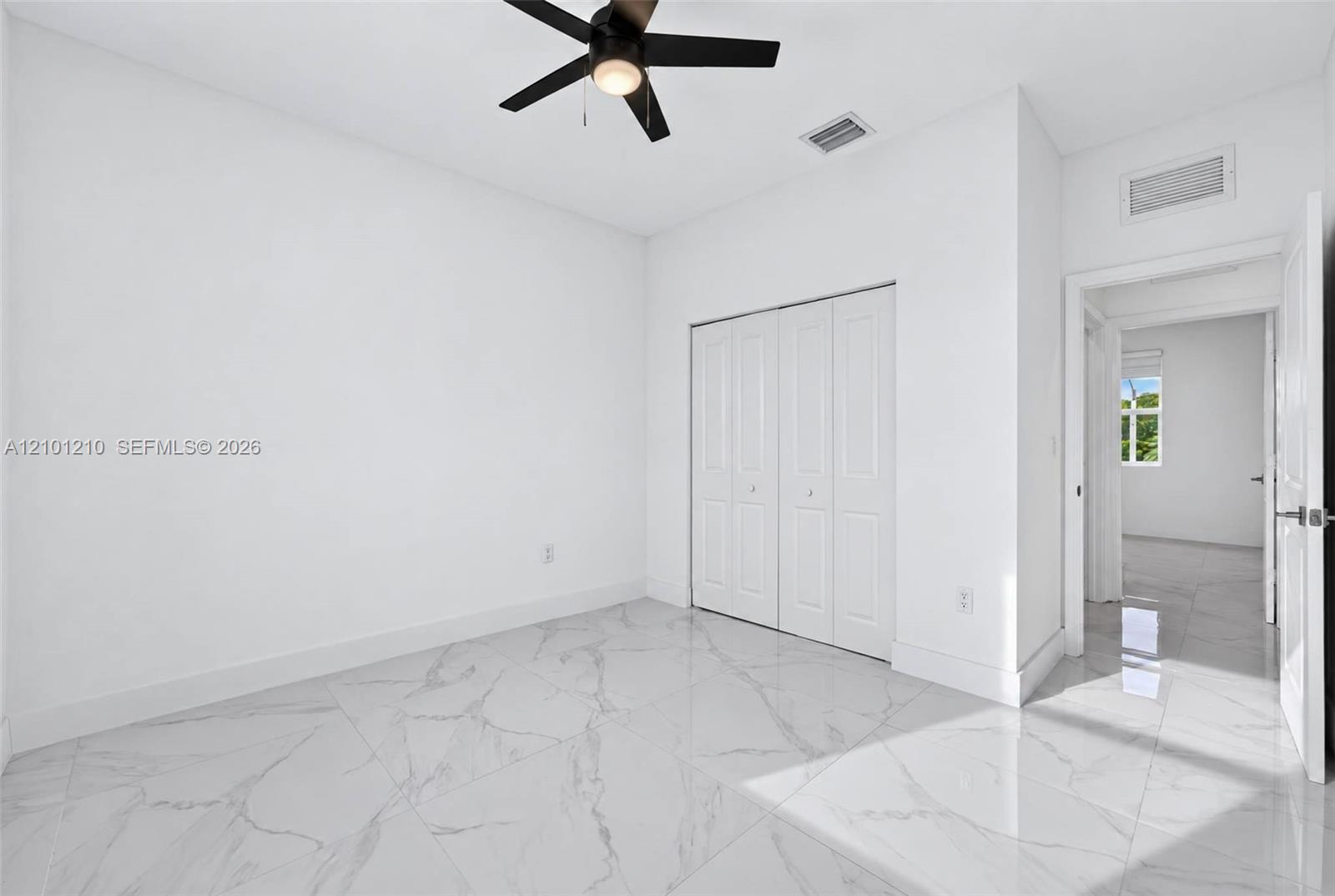 Empty bedroom with glossy marble-look tile floors, white closet doors, and a black ceiling fan.