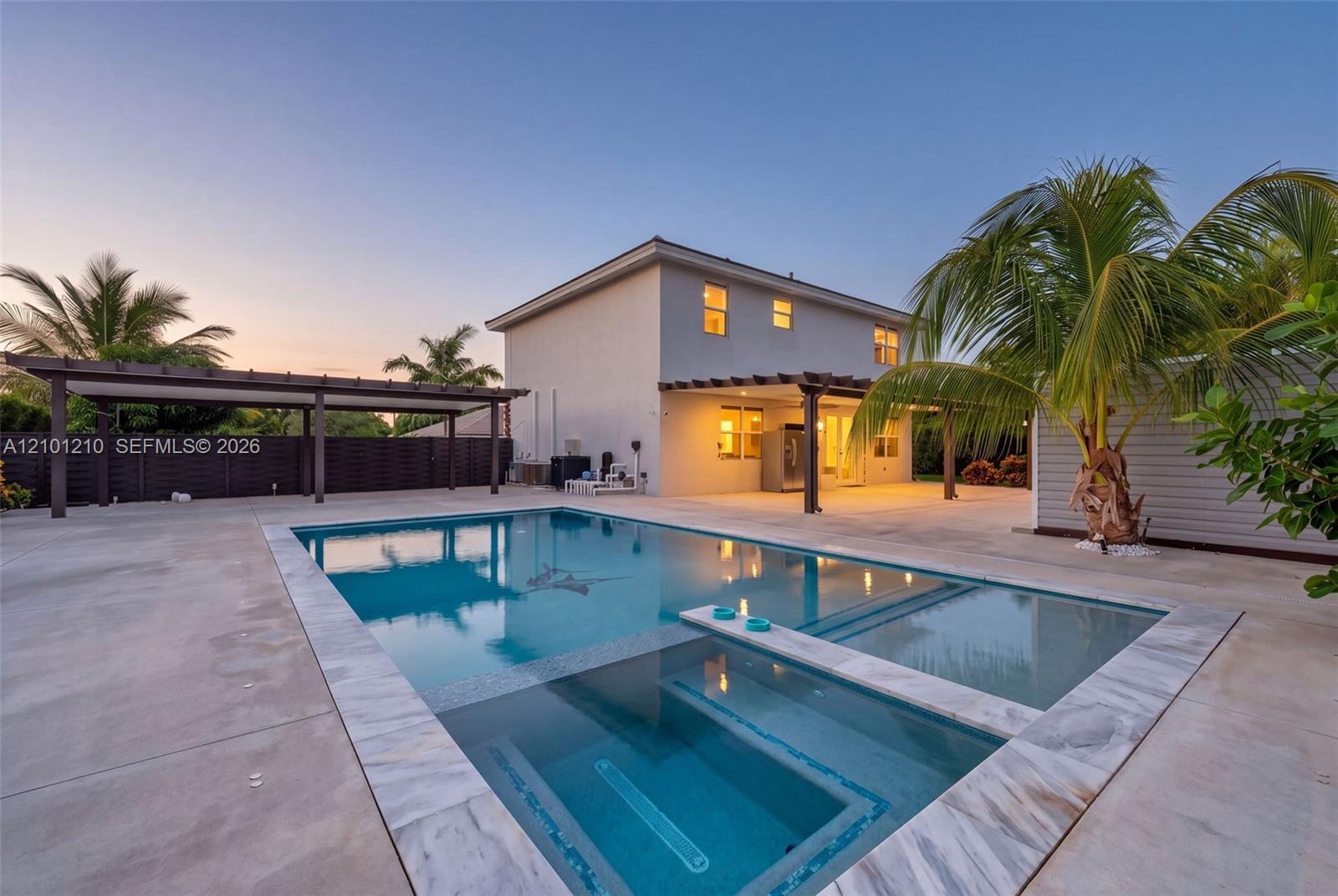 Modern two-story home with a geometric pool, covered patio, and palm trees at dusk.