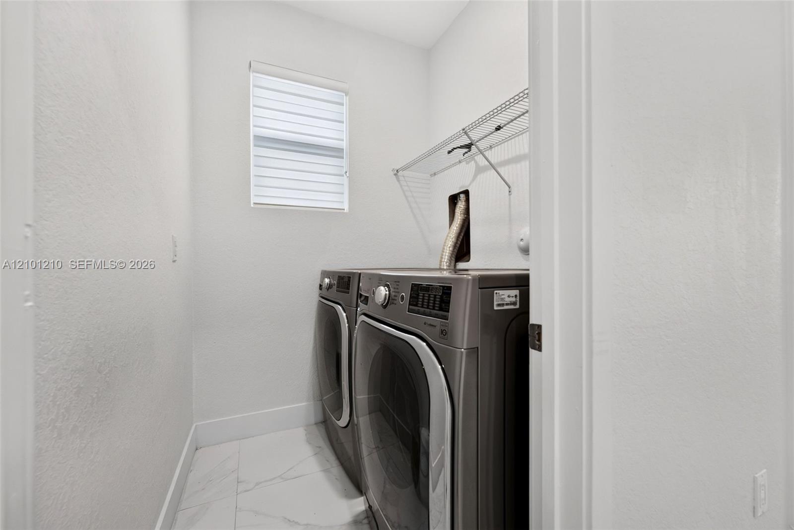 Laundry room with stainless front-loading washer and dryer beneath a wire shelf.