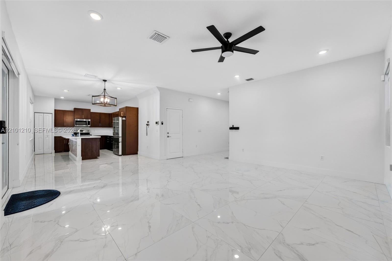Open-plan living area and kitchen with glossy marble-look floors, dark cabinetry, and a black ceiling fan.