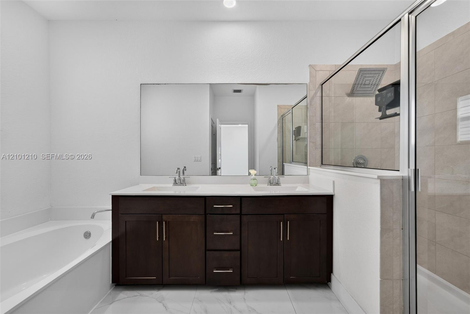 Bathroom with a dark double vanity, corner soaking tub, and glass-enclosed tiled shower.