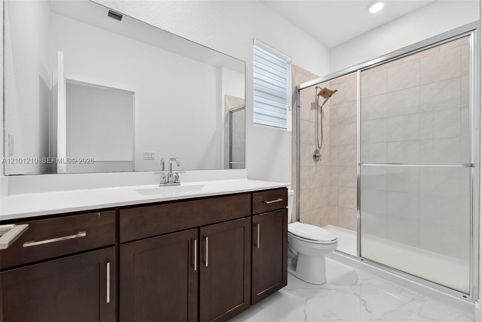 Bathroom with dark wood vanity, large mirror, and glass-enclosed tiled shower.