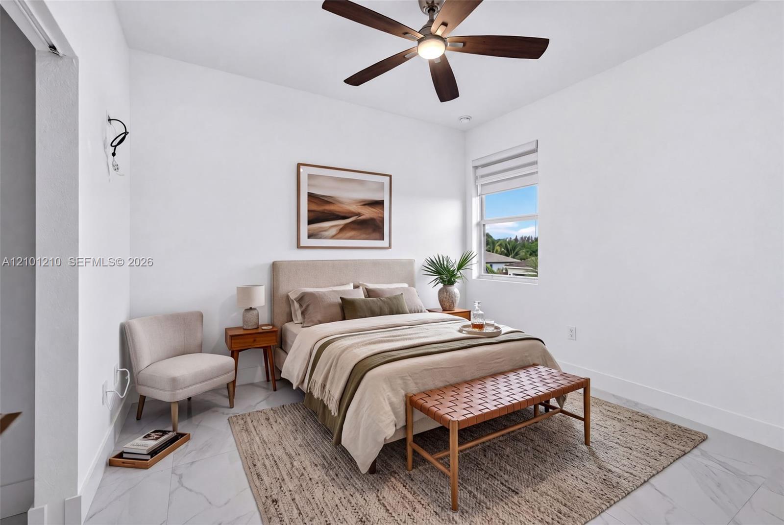 Staged bedroom with a neutral upholstered bed, woven bench, and ceiling fan.