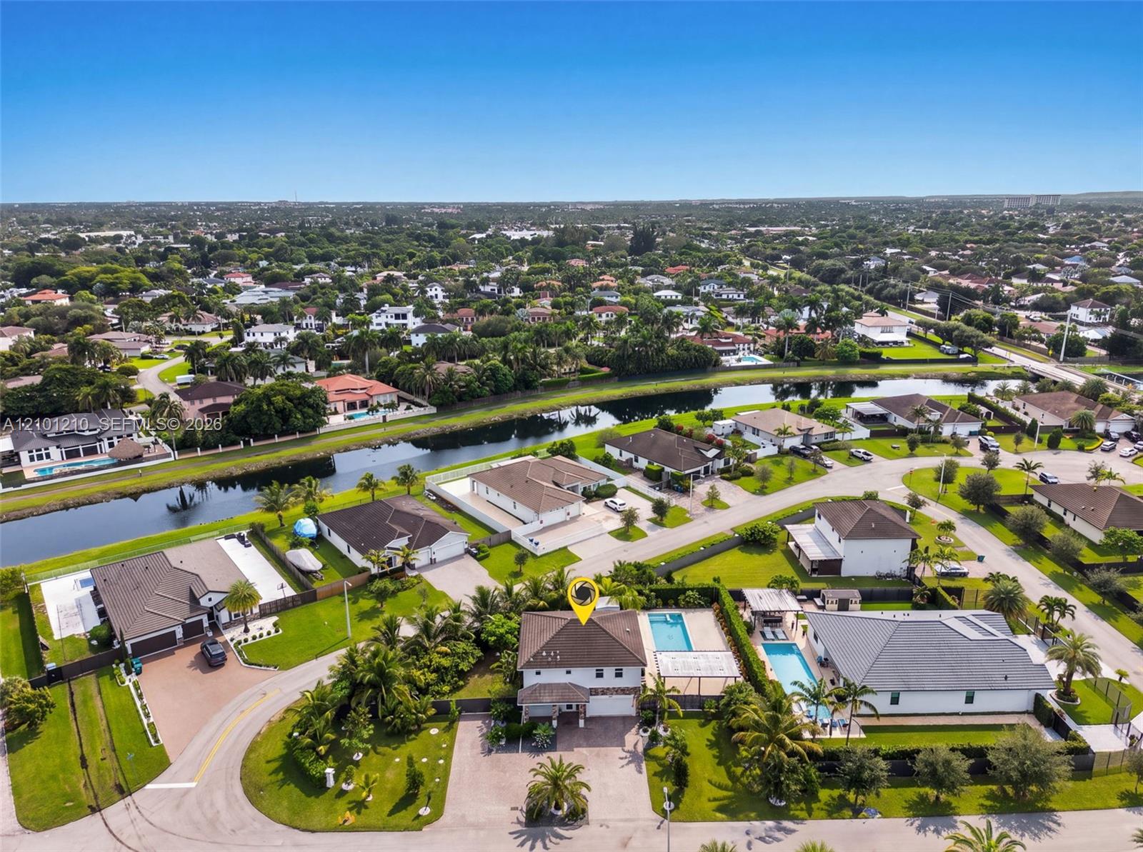 Aerial view of a canal-side neighborhood, with a yellow marker highlighting a home beside a pool.